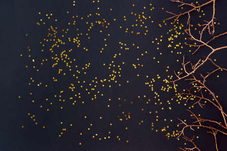 Flat lay border with gold christmas branch and golden confetti on a dark background