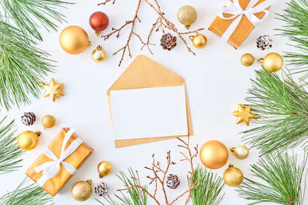 Mockup white greeting card and envelope with gold christmas balls, pine branches and gift box on a white backgroundの写真素材