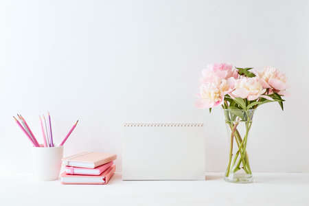 Mockup with a blank desk calendar and pink peonies in a vase on a white backgroundの写真素材