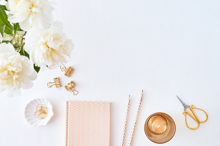 Flat lay blogger or freelancer workspace with a notebook and white peonies in a vase on a white tableの写真素材