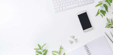 Flat lay home office desktop with keyboard, smartphone, notebook and green leaves on a white...