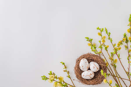 Flat lay composition with a willow branch, decorative nest with easter eggs on a white background