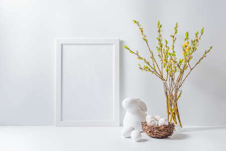 Home interior with easter decor. Mockup with a white frame and willow branches in a vase on a light backgroundの写真素材
