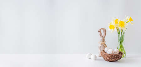 Home interior with easter decor. Yellow daffodils in a glass vase, easter eggs on a light backgroundの写真素材