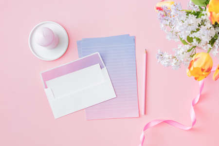 Mockup white wedding invitation and envelope with yellow tulips branches of lilac on a pink backgroundの写真素材