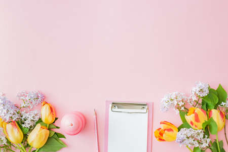 Flat lay blogger or freelancer workspace with a clipboard and yellow tulips branches of lilac on a pink backgroundの写真素材