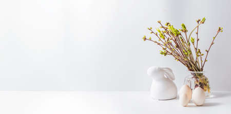 Home interior with easter decor. Green buds on branches in a glass vase, easter eggs on a light backgroundの写真素材