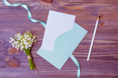 Mockup white wedding invitation and envelope with white flowers on a wooden background