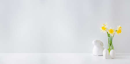 Home interior with easter decor. Yellow daffodils and easter eggs in a vase on a light backgroundの写真素材