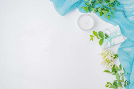Flat lay festive composition with scarf, white flowers, branches with green leaves on white backgroundの写真素材