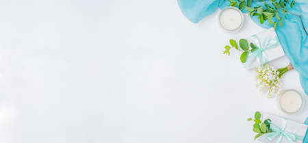 Flat lay festive composition with scarf, white flowers, branches with green leaves on white...