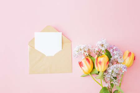 Mockup white greeting card and envelope with branches of lilac and yellow tulips on a pink...