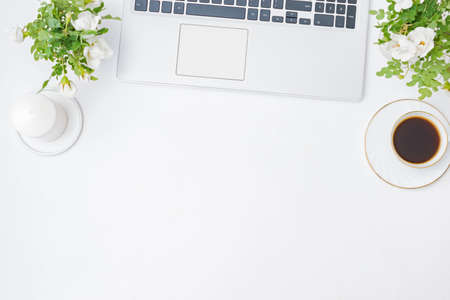 Flat lay blogger or freelancer workspace with a laptop, cup of coffee, small flowers and green leaves on a light backgroundの写真素材