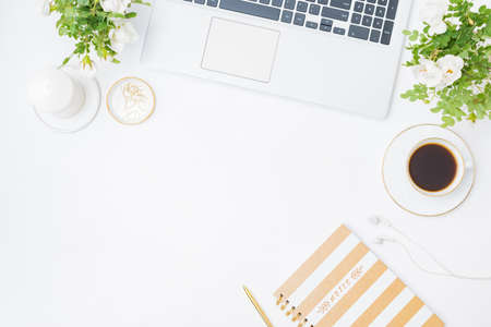 Flat lay blogger or freelancer workspace with a laptop, cup of coffee, small flowers and green...