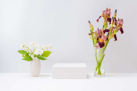 Empty white box and bouquet of irises flowers in a glass vase on a light background. Mockup banner for display of advertise productの写真素材