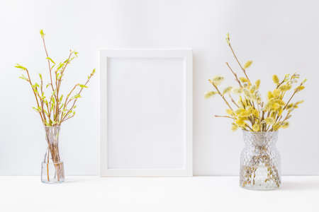 Home interior with easter decor. Mockup with a white frame and willow branches in a vase on a light backgroundの写真素材