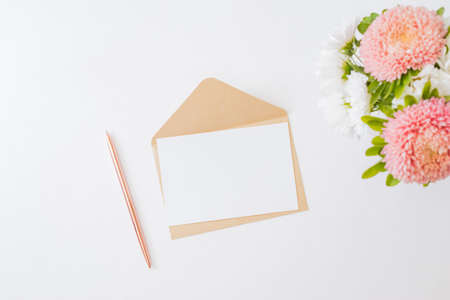 Mockup white greeting card and envelope with white and pink flowers in a vase on a light backgroundの写真素材