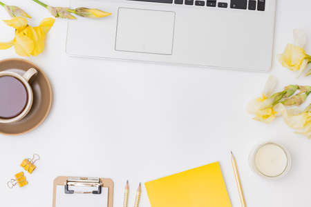 Flat lay home office desktop with laptop, yellow irises, cup with coffee on a white backgroundの写真素材