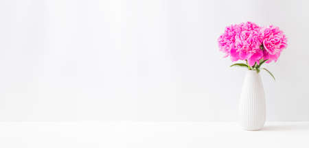 Minimalist home interior with decor elements. Pink peonies in a vase on a light backgroundの写真素材