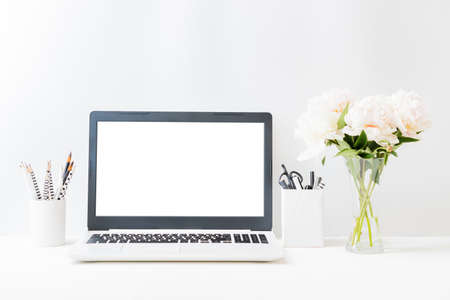 Home office workspace with laptop mockup and white peonies in a vase, office supplies on a light backgroundの写真素材