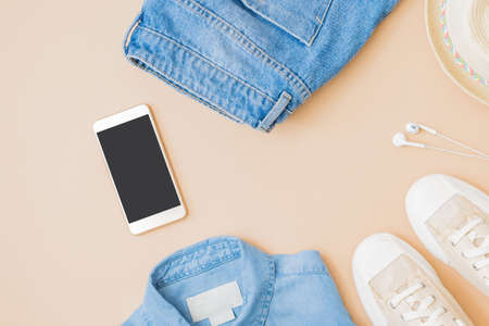 Flat lay summer composition with a straw hat, jeans and sneakers on a yellow background