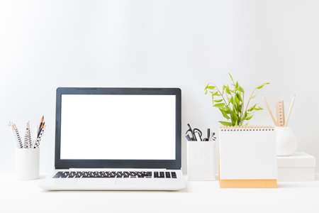 Home office workspace with laptop mockup and branches with green leaves in a vase, office supplies, desk calendar on a light backgroundの写真素材