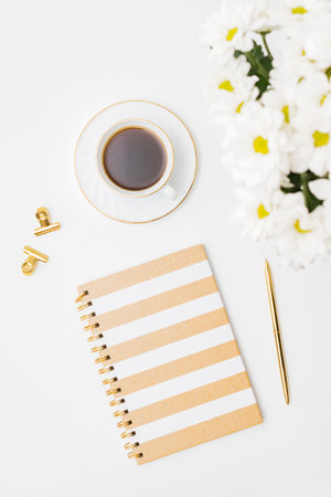 Flat lay home office desktop with notebook, white flowers, cup of coffee on a white backgroundの写真素材