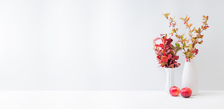 Home interior decor elements. Colorful autumn leaves and red berries in a vase on a light backgroundの写真素材
