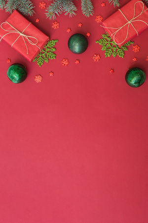 Flat lay frame with fir branches, christmas baubles decoration and gift box on a red backgroundの写真素材