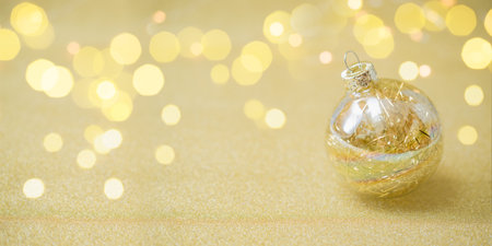 Golden christmas ball on golden shiny abstract background and blurred bokehの写真素材