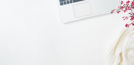 Minimalistic flat lay composition with laptop and branches with red berries, white sweater on a...