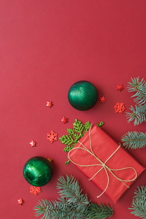 Flat lay frame with fir branches, christmas baubles decoration and gift box on a red backgroundの写真素材
