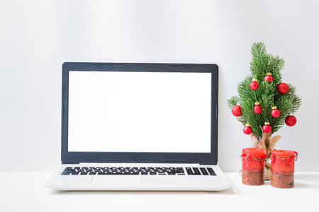 Office workspace with laptop mockup screen, christmas tree, candle, supplies on a light background. Christmas home interior or office backgroundの写真素材