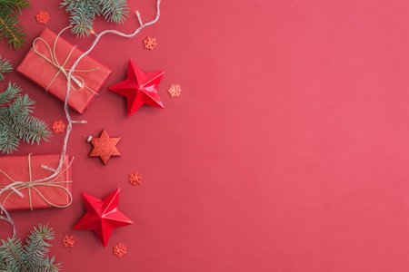 Flat lay frame with fir branches, christmas baubles decoration and gift box on a red backgroundの写真素材