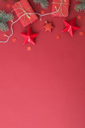 Flat lay frame with fir branches, christmas baubles decoration and gift box on a red backgroundの写真素材