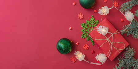 Flat lay frame with fir branches, christmas baubles decoration and gift box on a red backgroundの写真素材
