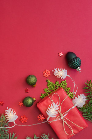 Flat lay frame with fir branches, christmas baubles decoration and gift box on a red backgroundの写真素材