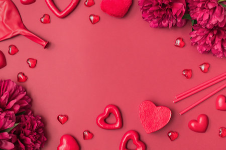 Flat lay valentines day frame with red peonies, paper drinking straws and red hearts on a red background. Valentines day banner with copy spaceの写真素材