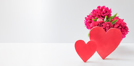 Red peonies and red heart on a white table with copy space. Flowers composition for Valentine's, Mothers or Women's Day.の写真素材
