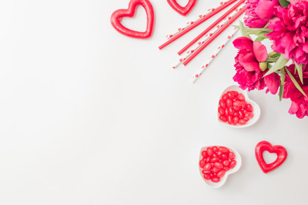 Flat lay valentines day frame with red peonies, candies and red hearts on a white background. Valentines day banner with copy spaceの写真素材