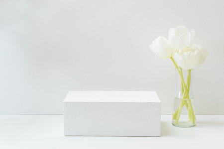 Geometric podium or pedestal with white spring tulips in a vase on a white background. Empty podium for product presentationの写真素材