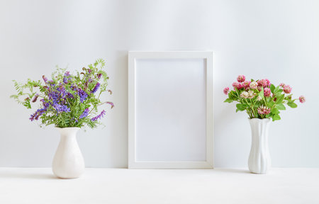 Home interior decor elements. Mockup with a white frame and wildflowers in a vase on a light backgroundの写真素材