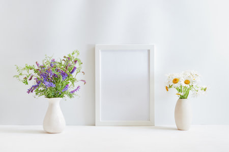 Home interior decor elements. Mockup with a white frame and wildflowers in a vase on a light backgroundの写真素材