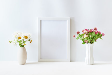 Home interior decor elements. Mockup with a white frame and wildflowers in a vase on a light backgroundの写真素材