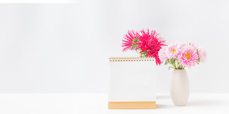 Mockup white desk calendar and pink flowers in a vase on a light background. Spiral calendar mockup template advertising and brandingの写真素材