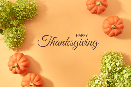 Flat lay autumn frame with green flowers and pumpkins on an orange background. Happy thanksgiving message for holidayの写真素材