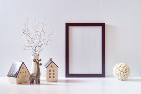 Mock up black poster frame with Christmas decoration in home interior, scandinavian style. Christmas little house, deer and ball on a white tableの写真素材