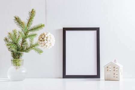 Mock up poster frame with christmas decoration in home interior, scandinavian style. Green fir branches in a vase on a white tableの写真素材