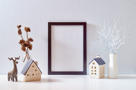 Mock up black poster frame with Christmas decoration in home interior, scandinavian style. Christmas little house and deer on a white tableの写真素材