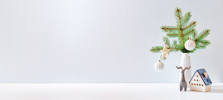 Christmas, New Year home decor. Empty white wall mock up with green fir branches in a vase, Christmas little house and deer on a white table. Mock up for display worksの写真素材